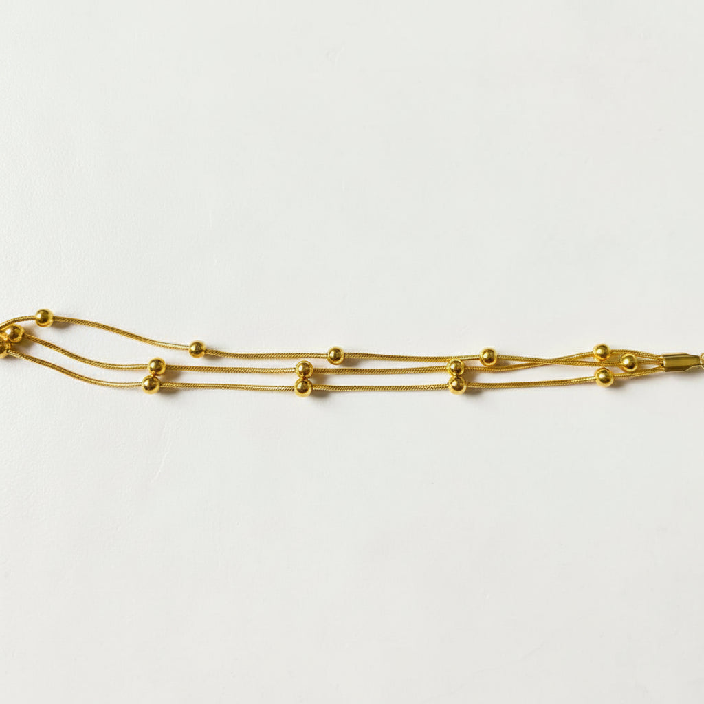 Altin Noor gold-tone multi-strand snake chain bracelet with polished beads on a textured white surface.