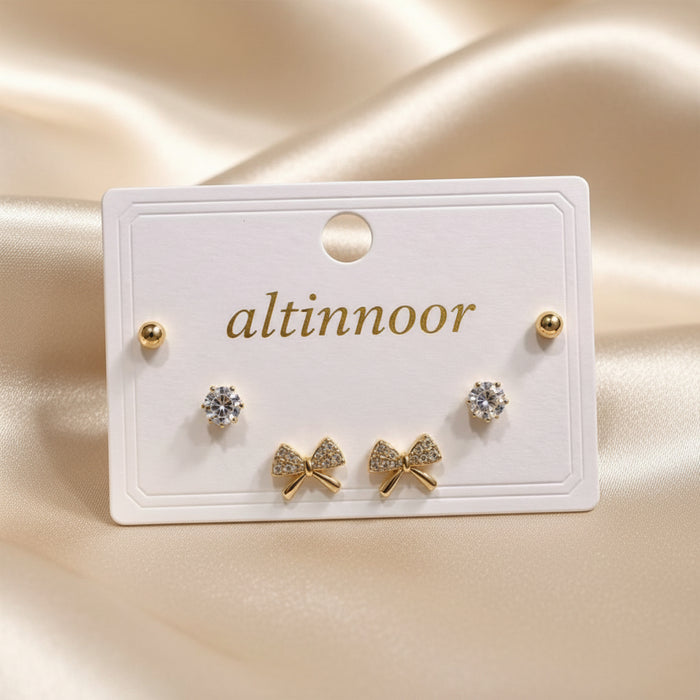 Altin Noor earring set featuring gold-tone ball studs, solitaire cubic zirconia, and crystal-encrusted bow studs.
