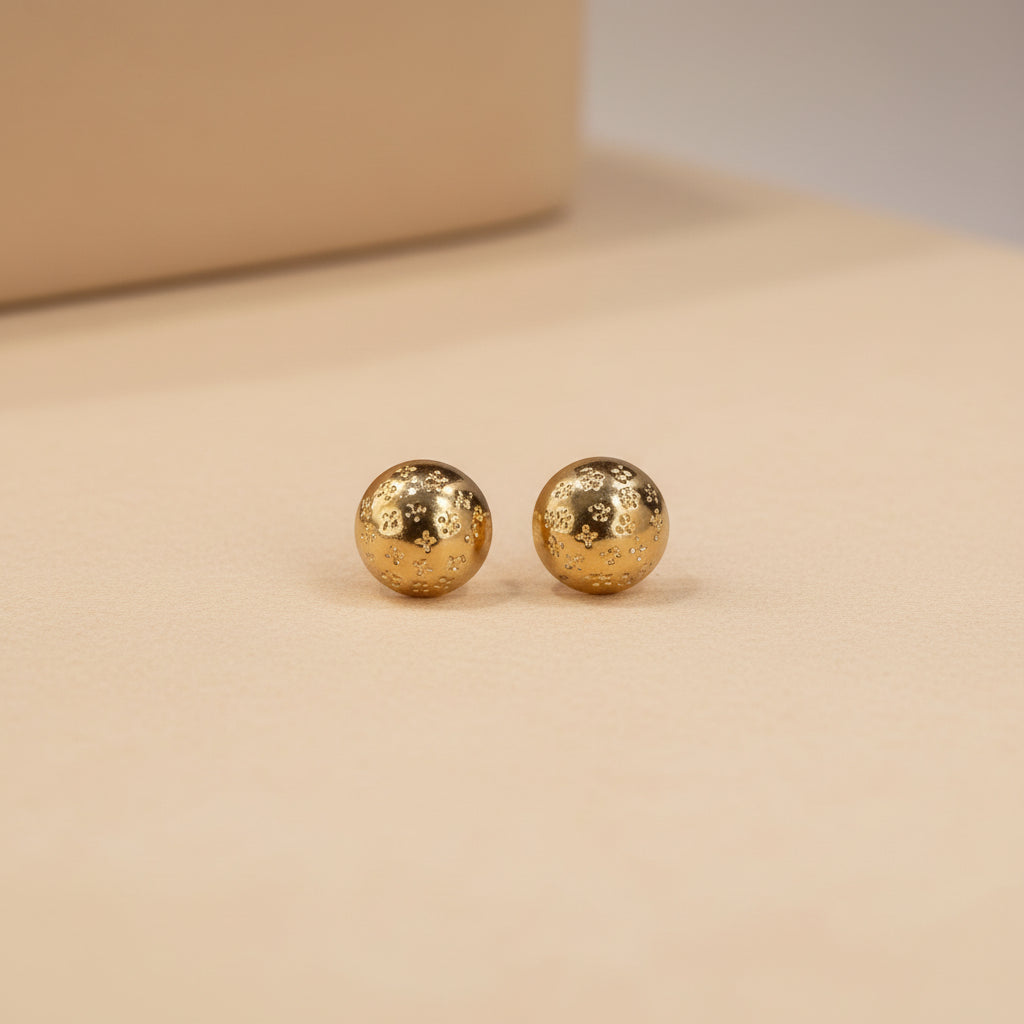 Altin Noor gold-tone dome stud earrings with intricate embossed patterns held in a palm against a grey background.