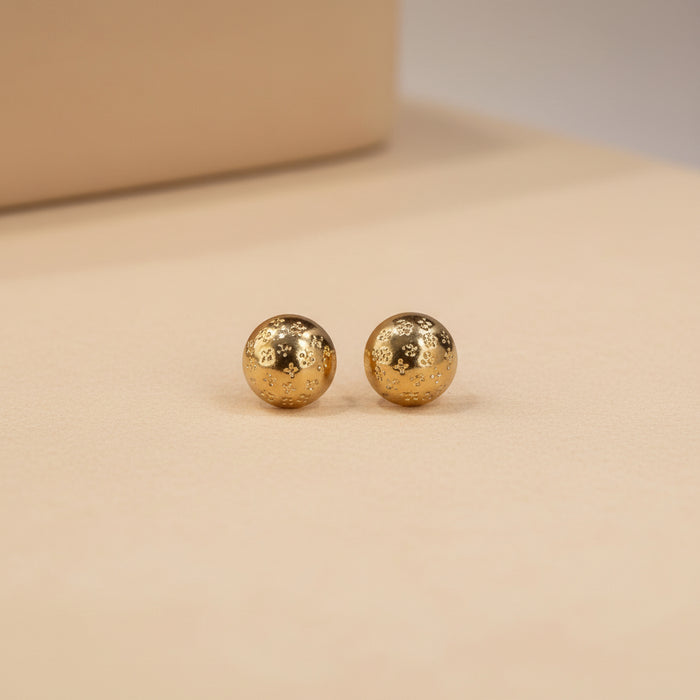Altin Noor gold-tone dome stud earrings with intricate embossed patterns held in a palm against a grey background.