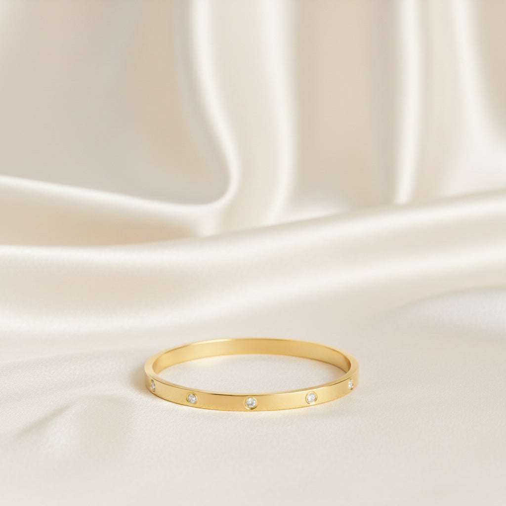 Altin Noor gold-tone metal bangle bracelet featuring flush-set cubic zirconia stones on a polished minimalist band
