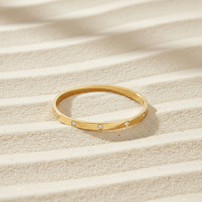 Altin Noor gold-tone metal bangle bracelet featuring flush-set cubic zirconia stones on a polished minimalist band