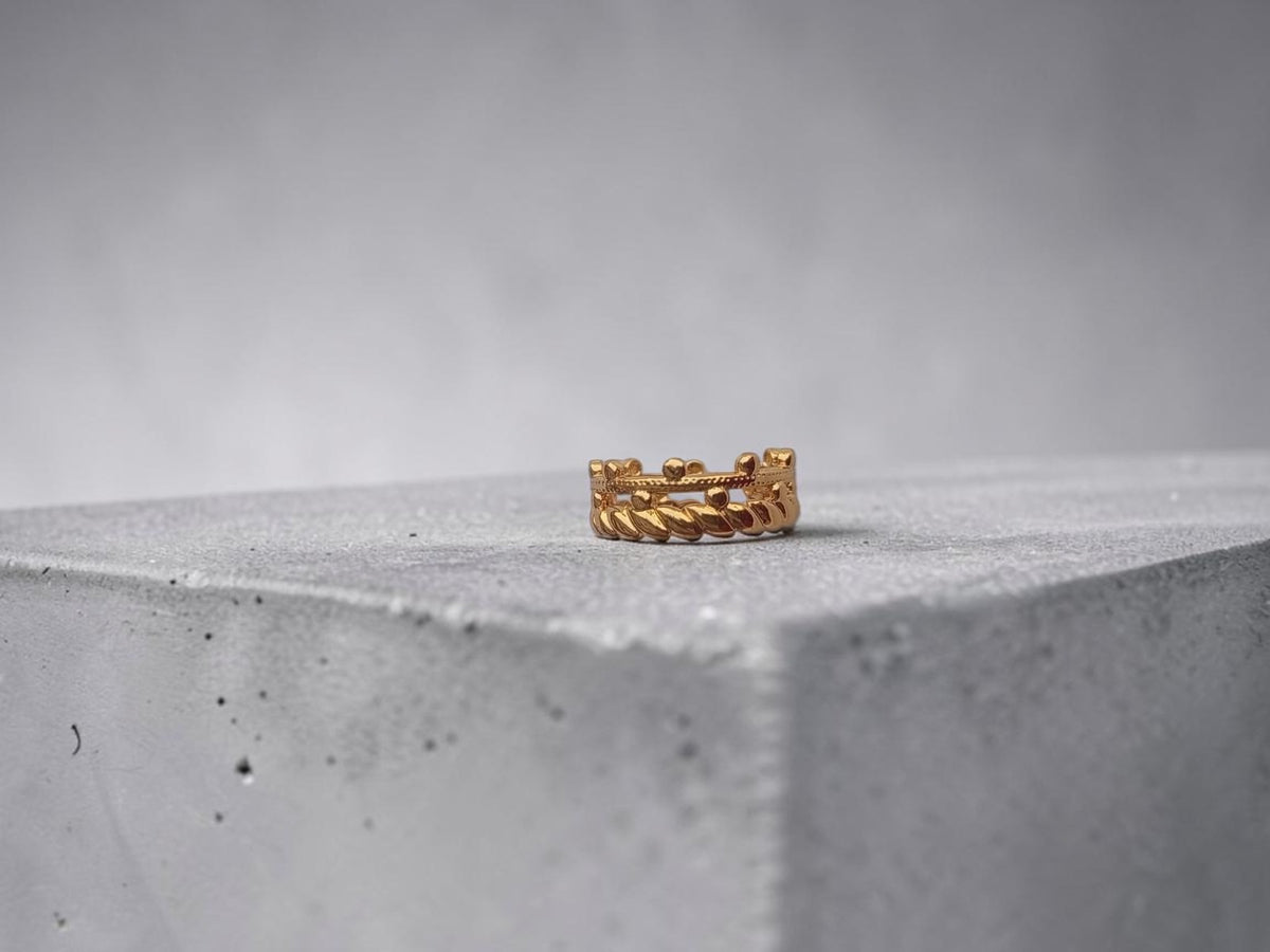 Altin Noor gold-tone stackable ring featuring a beaded band and twisted rope texture on a grey concrete block