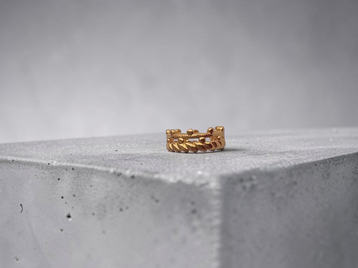 Altin Noor gold-tone stackable ring featuring a beaded band and twisted rope texture on a grey concrete block
